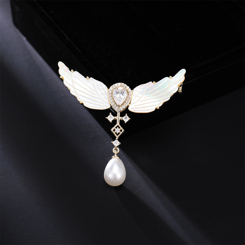 Angel wings mother-of-pearl brooch with pearl drop on dark background