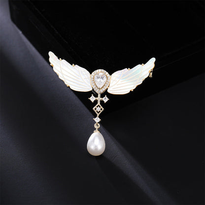 Angel wings mother-of-pearl brooch with pearl drop on dark background